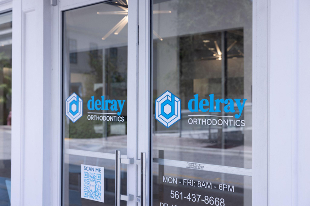 Delray Orthodontics storefront entrance with glass doors and blue logo signage