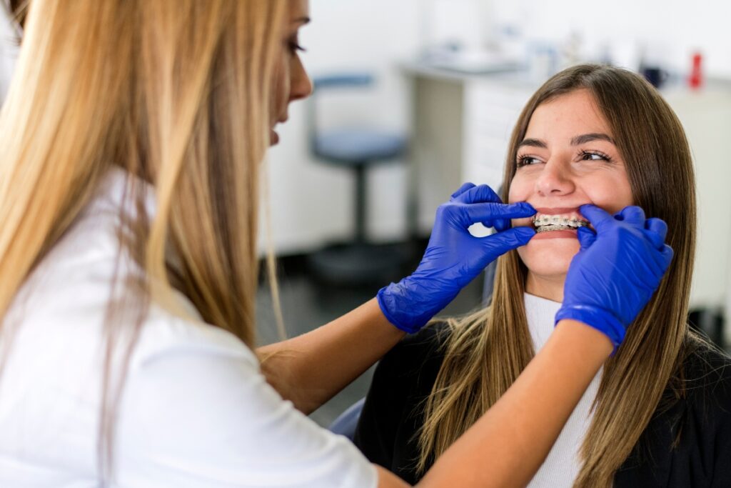 Orthodontist examining patient's teeth wearing blue gloves in dental office.