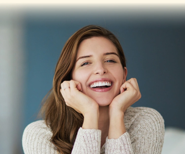 Happy woman in gray sweater smiling with hands to face against blue background